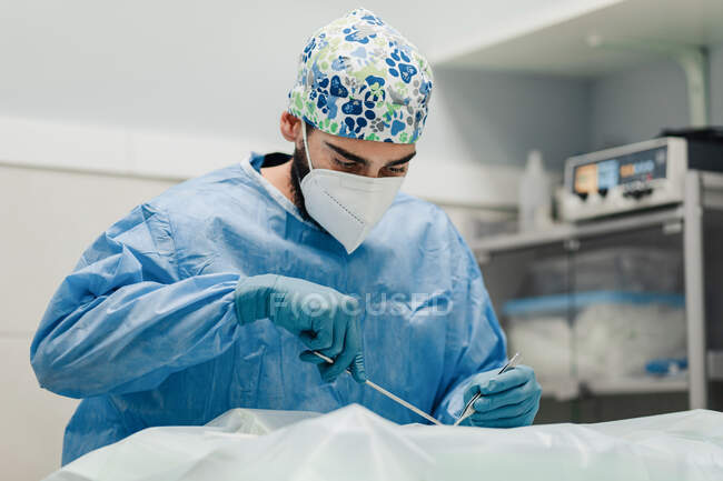 Зосереджений ветеринар чоловічої статі в уніформі та дихальній масці з використанням медичних інструментів під час операції в лікарні — стокове фото