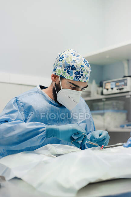 Зосереджений ветеринар чоловічої статі в уніформі та дихальній масці з використанням медичних інструментів під час операції в лікарні — стокове фото