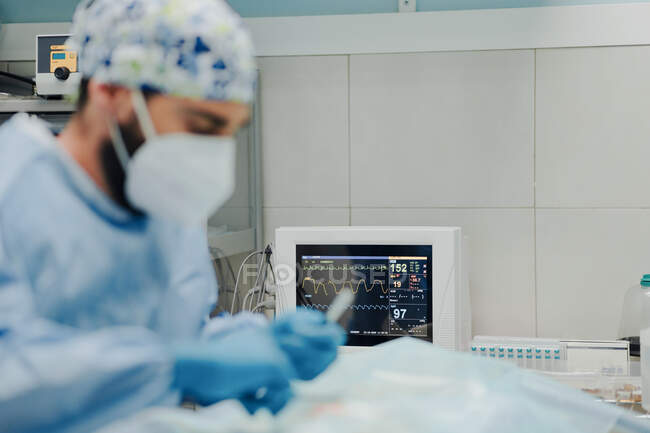 Veterinario masculino enfocado en máscara uniforme y respiratoria utilizando instrumentos médicos durante la cirugía en el hospital - foto de stock