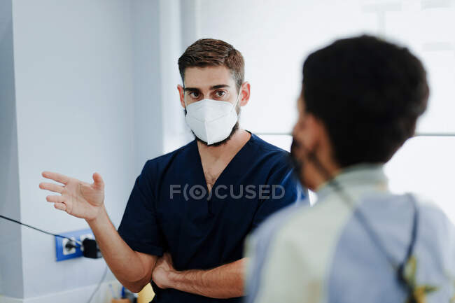 Médicos varones anónimos atentos con máscaras y uniformes médicos que hablan en el trabajo en el hospital - foto de stock
