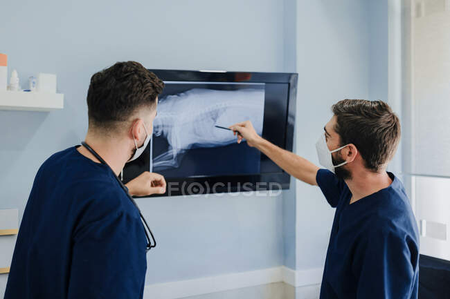Бічний вид нерозпізнаних чоловічих веж у масках, які взаємодіють під час спостереження за монітором з рентгенівським зображенням у лікарні. — стокове фото