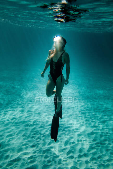 Стройная женщина в купальниках и ластах плавает под водой в бирюзовом море — стоковое фото