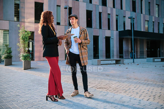 Young black businesswoman with tablet talking to male colleague with takeaway coffee while looking at each other in town — Stock Photo
