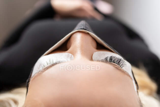 Detail of artificial eyelashes on young female client wearing protective face mask in modern beauty studio — Stock Photo