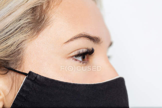 Colheita calma jovem fêmea em máscara facial preta com pestanas permanentes extensão no olho direito olhando para longe — Fotografia de Stock