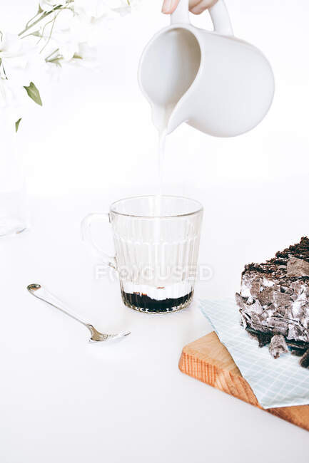 Cultivo persona anónima verter leche fresca caliente en el vaso con dulce derretimiento helado de chocolate en la cocina ligera - foto de stock