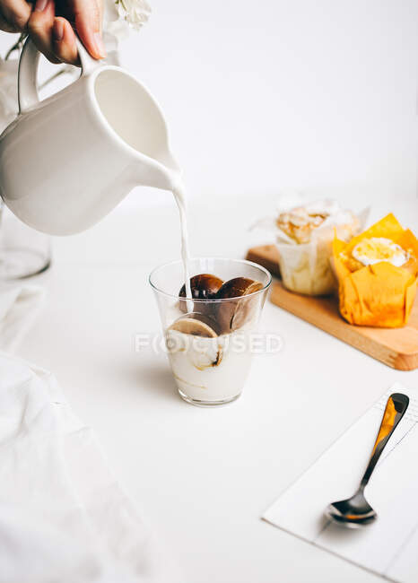 Crop anonyme Person, die heiße Milch in Glas mit köstlichen schmelzenden Schokoladenbomben auf dem Tisch in der Nähe von süßen Cupcakes platziert — Stockfoto