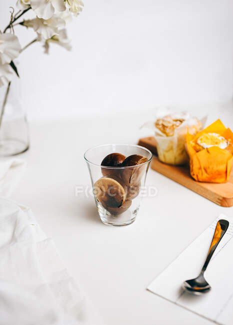 Zusammensetzung von süßen Schokoladenbomben, die in einem Glas frischer heißer Milch schmelzen, das auf den Tisch neben leckeren Cupcakes und Milchkannen gelegt wird — Stockfoto