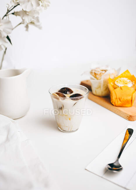 Composition of sweet chocolate bombs melting in glass of fresh hot milk placed on table near yummy cupcakes and milk jug — Stock Photo