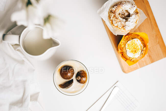Top view composition of sweet chocolate bombs melting in glass of fresh hot milk placed on table near yummy cupcakes and milk jug — Stock Photo