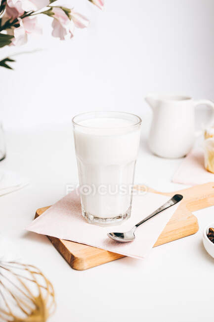 Fresh warm milk from jug into glass placed on cutting board in light kitchen — Stock Photo