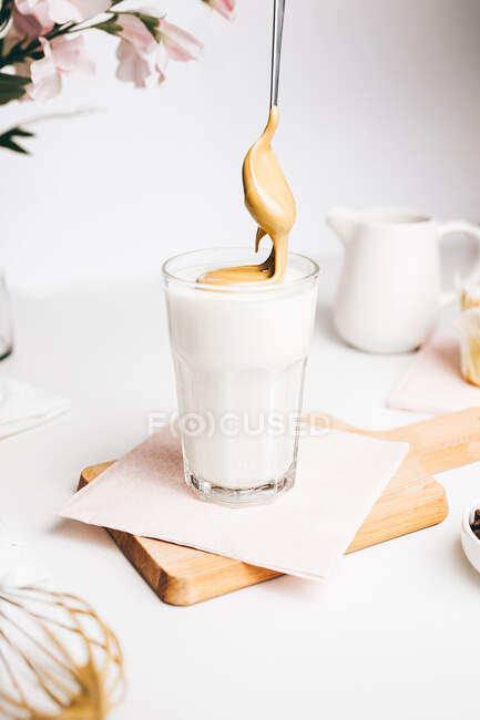 Teaspoon with sweet whipped foam above fresh yummy latte served on wooden cutting board in modern light kitchen — Stock Photo