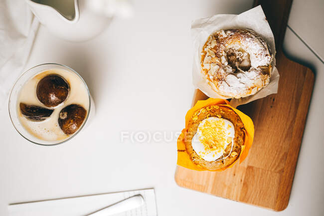 Top view composition of sweet chocolate bombs melting in glass of fresh hot milk placed on table near yummy cupcakes and milk jug — Stock Photo