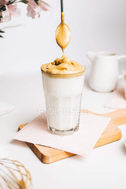 Colher de chá com espuma batida doce acima do leite gostoso fresco servido na placa de corte de madeira na cozinha leve moderna — Fotografia de Stock