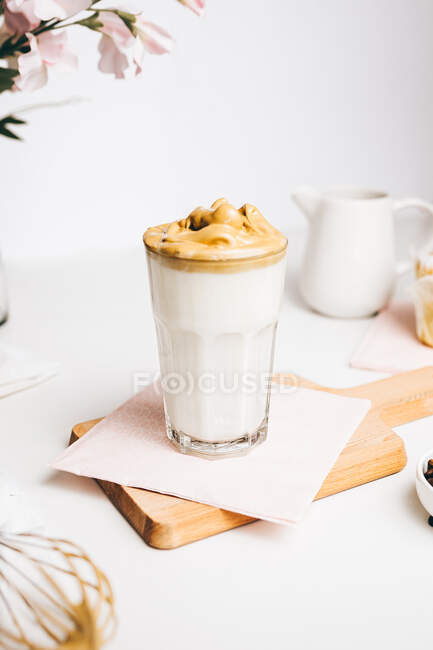 Cuillère à café avec de la mousse fouettée douce au-dessus de latte fraîche délicieuse servie sur une planche à découper en bois dans une cuisine moderne et légère — Photo de stock