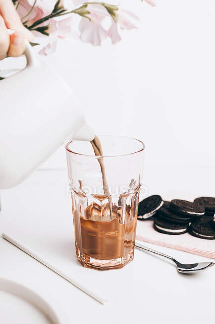 Cultivar pessoa anônima derramando leite de chocolate quente em vidro com biscoitos doces — Fotografia de Stock