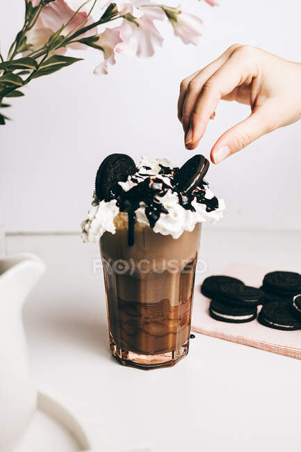 Ernte anonyme Person dekoriert süßen leckeren Frappé-Drink mit Schokoladenkeksen auf Schlagsahne in heller Küche — Stockfoto