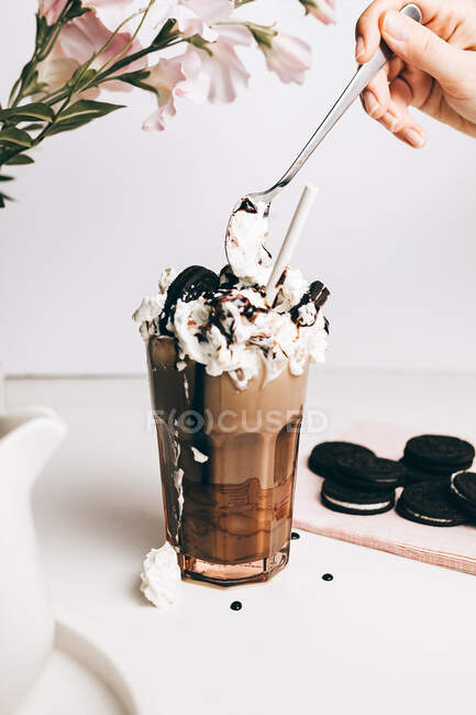 Cultivo persona anónima decoración dulce delicioso frappe bebida con galletas de chocolate en crema batida en la cocina ligera - foto de stock
