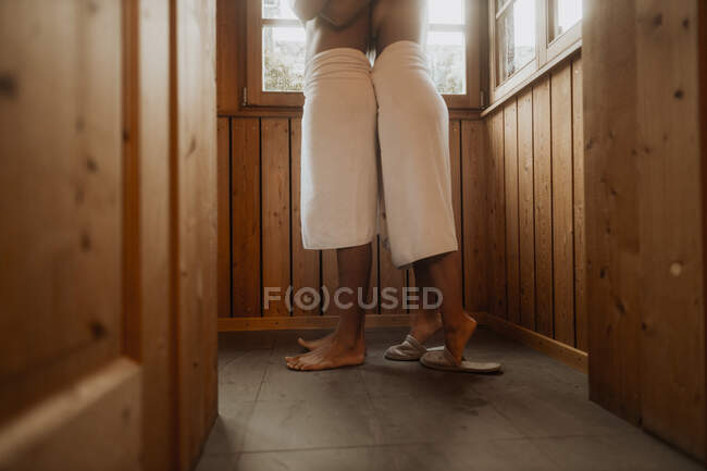 Vista lateral da cultura mulher anônima em chinelos abraçando namorado sem camisa em cabana de madeira enquanto passam o tempo juntos no fim de semana — Fotografia de Stock