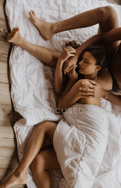 De conteúdo acima relaxado fêmea deitada em pernas de namorados em forma de cobertor acolhedor macio no chão de madeira — Fotografia de Stock