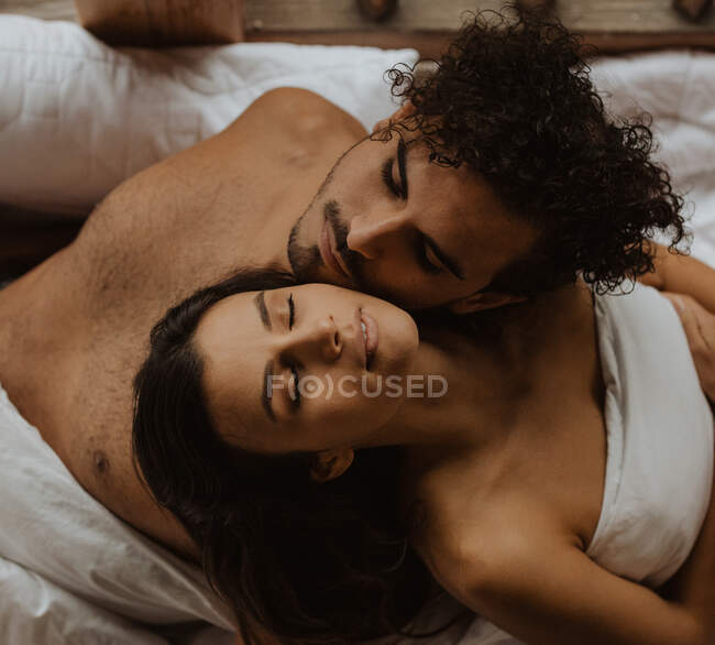 From above romantic young couple sitting back to back and resting heads on each others shoulders while relaxing with eyes closed on soft blanket — Stock Photo