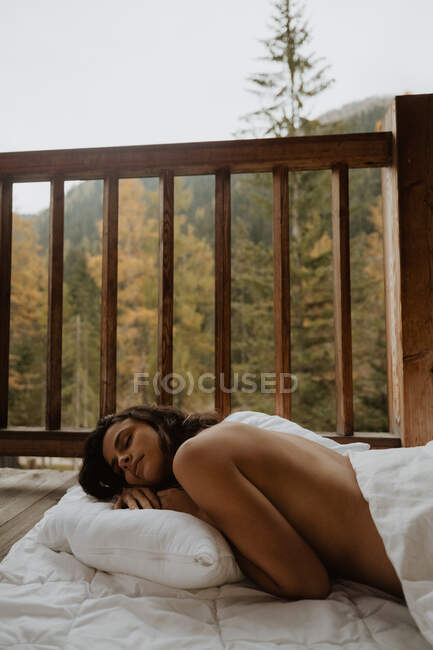 Вид збоку струнка красуня брюнетка спокійно спить на м'якій ковдрі на дерев'яному ганку проти листяного лісу в осінній день — стокове фото