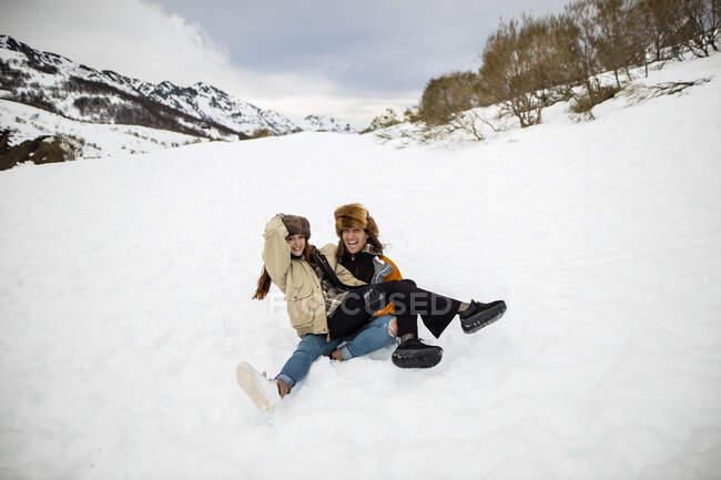 Young laughing male traveler with closed eyes sitting with female beloved on lap on snowy mount under cloudy sky in Spain — Stock Photo