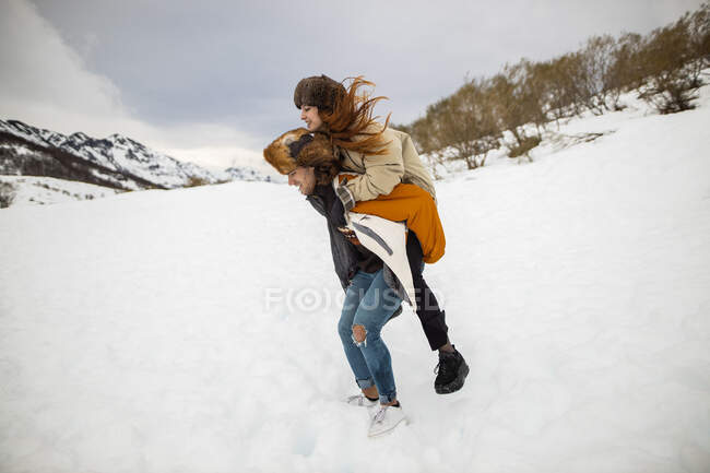 Вид збоку веселого чоловічого туриста, що носить дівчину в скарбничці на засніженій горі взимку — стокове фото