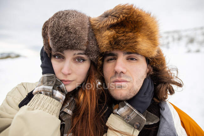 Jeune couple de voyageurs en vêtements de dessus debout contre le mont tout en regardant la caméra en hiver dans les Asturies — Photo de stock