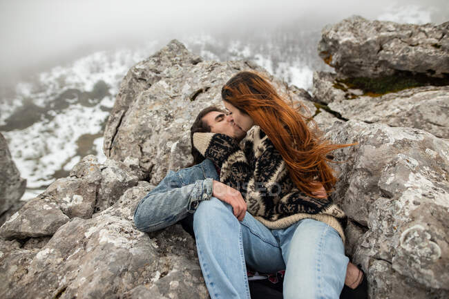 Young female traveler kissing boyfriend with closed eyes while spending time on mount in wintertime on misty day — Stock Photo