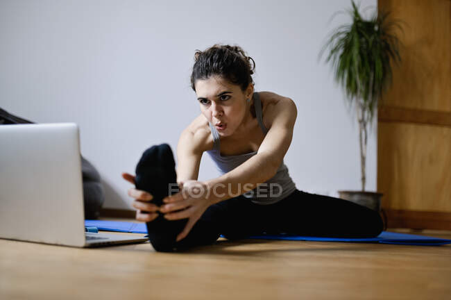 Adult focused sportswoman leaning forward during workout with video tutorial on netbook at home — Stock Photo
