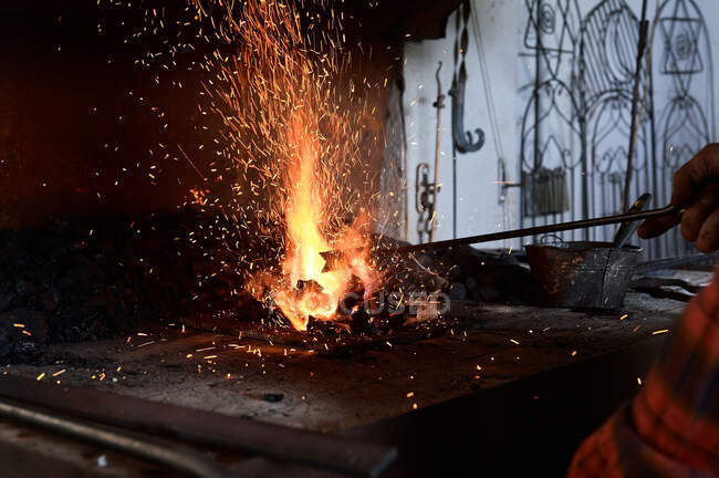 Ernte bis zur Unkenntlichkeit männlicher Schmied erhitzt Metallstange auf brennender Flamme während Schmiedeprozess in Werkstatt — Stockfoto