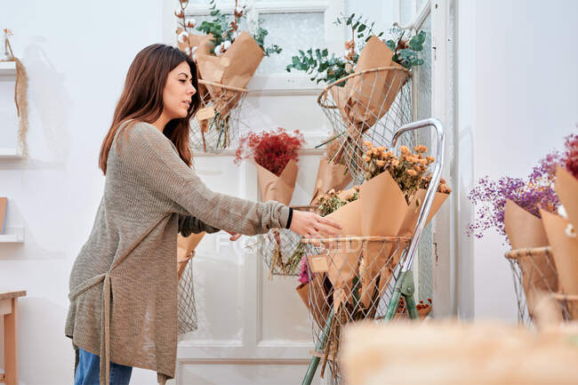 Side view of female client taking bouquet of flowers from container while making choice in shop — Stock Photo