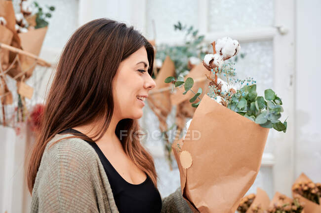 Вид сбоку на клиентку цветочного магазина, нюхающую букет цветов, завернутых в бумажный пакет — стоковое фото