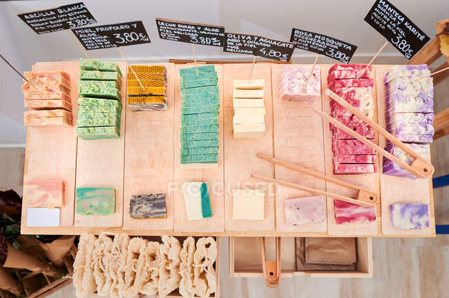 Desde arriba de varios jabón hecho a mano de colores con pinzas y etiquetas de precios colocados en la mesa de madera en eco tienda - foto de stock