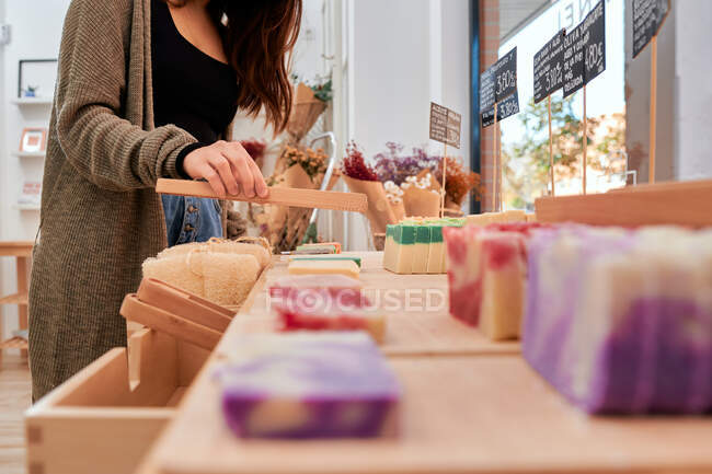 Cosecha anónima comprador femenino recoger jabón hecho de ingredientes naturales mientras que las compras en la tienda con productos ecológicos - foto de stock