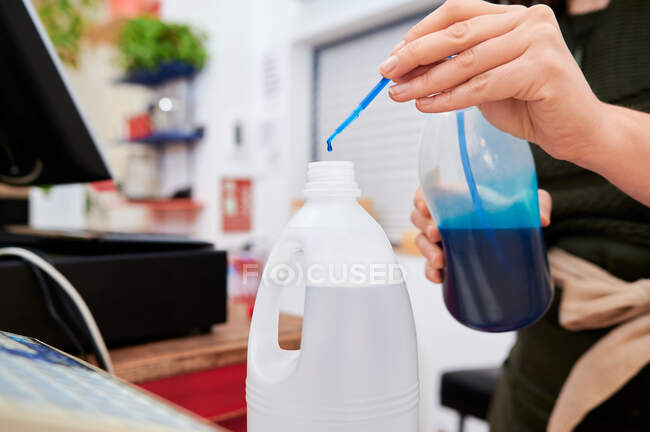 Cultivada vendedora irreconhecível na loja com engarrafamento eco detergentes despejando limpador enquanto prepara a ordem do cliente no balcão — Fotografia de Stock