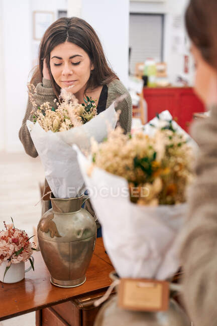 Клиентка цветочного магазина, нюхающая букет цветов, завернутый в бумажный пакет с закрытыми глазами — стоковое фото
