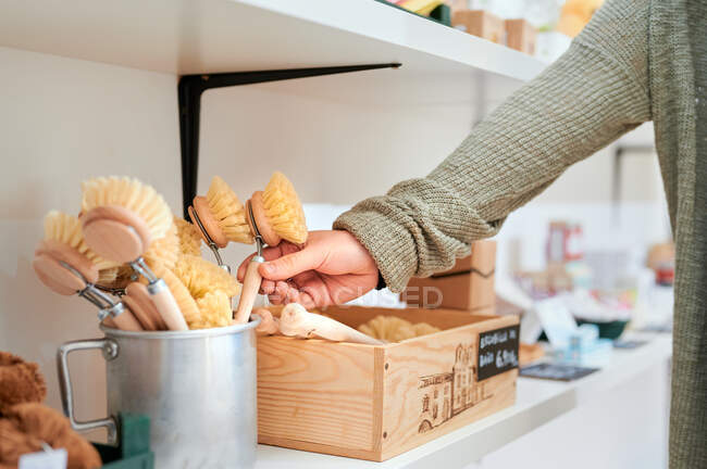 Анонимная женщина-клиент берет деревянную щетку из контейнера во время покупок в нулевом магазине отходов — стоковое фото