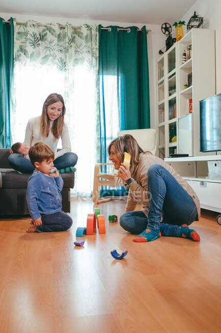 Sorrindo mulher brincando com filho no quarto com parceiro homossexual sentado com bebê no sofá — Fotografia de Stock