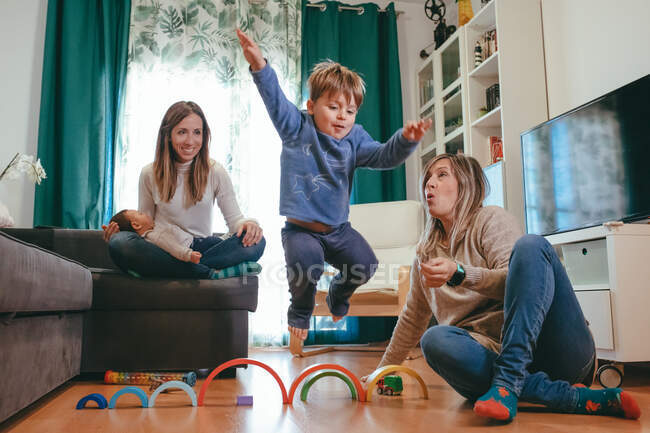 Full length excited young lesbian couple wearing casual clothes playing with adorable little kids while spending free time in modern living room — Stock Photo