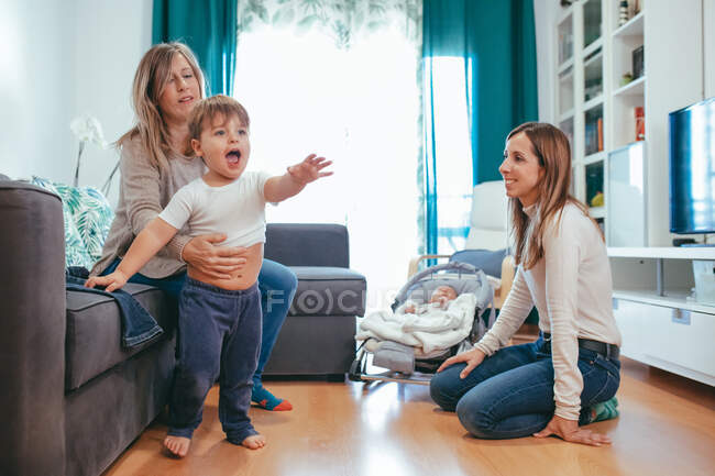 Sonriente joven pareja lesbiana jugando con adorables niños pequeños mientras pasan tiempo libre juntos en la moderna sala de estar - foto de stock