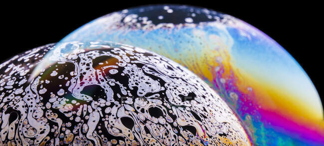 Vista panorámica del fondo texturizado de la burbuja de primer plano que representa planetas coloridos con líneas onduladas en la superficie en forma redonda sobre fondo negro - foto de stock