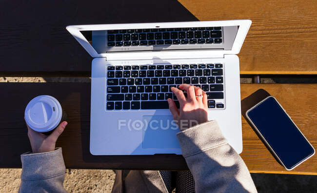 Top view of unrecognizable young woman using her laptop on the street at a table while having coffee — Stock Photo