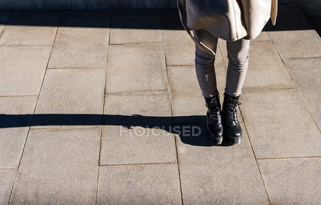 De cima da colheita fêmea irreconhecível em botas e casaco quente em pé na calçada pavimentada no dia ensolarado de outono — Fotografia de Stock
