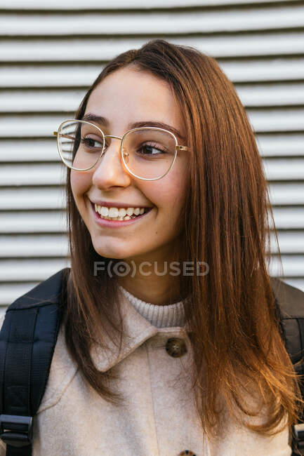Передній вид врожаю студентка-жінка в повсякденному одязі з рюкзаком, що стоїть на вулиці і дивиться в сторону з посмішкою — стокове фото