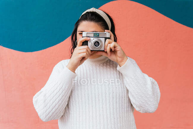 Anonimo focalizzato femminile in abbigliamento casual scattare foto sulla fotocamera digitale vicino a parete luminosa alla luce del giorno — Foto stock