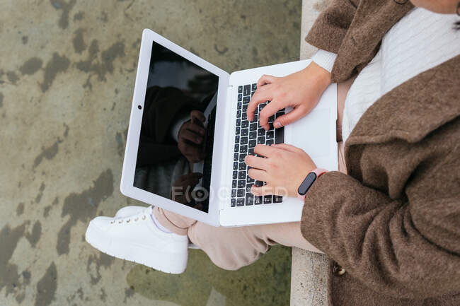 From above side view of crop anonymous plus size female surfing internet on netbook with black screen above pond in town — Stock Photo