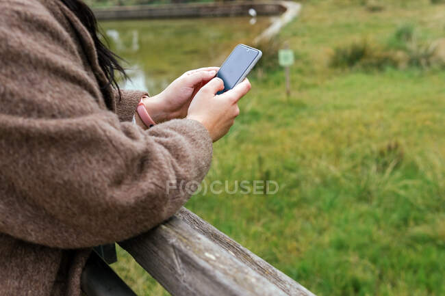 Corte de anônimo jovem gordinha fêmea no casaco de surf internet no celular na cidade — Fotografia de Stock