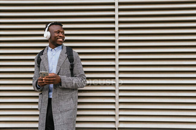 Side view of content African American male manager in headset text messaging on cellphone near wall in town — Stock Photo